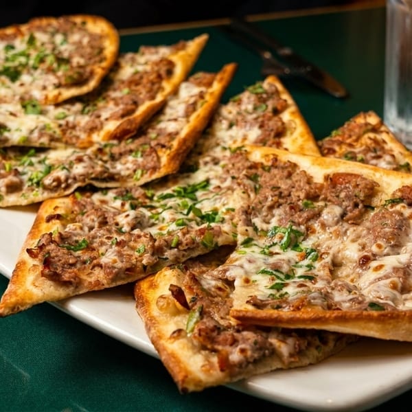 A white platter filled with several slices of meat and cheese flatbread on a green tablecloth.