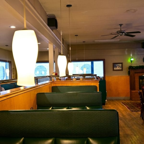 Cozy restaurant interior with green booths, wooden tables, a fireplace, and decorative lighting.